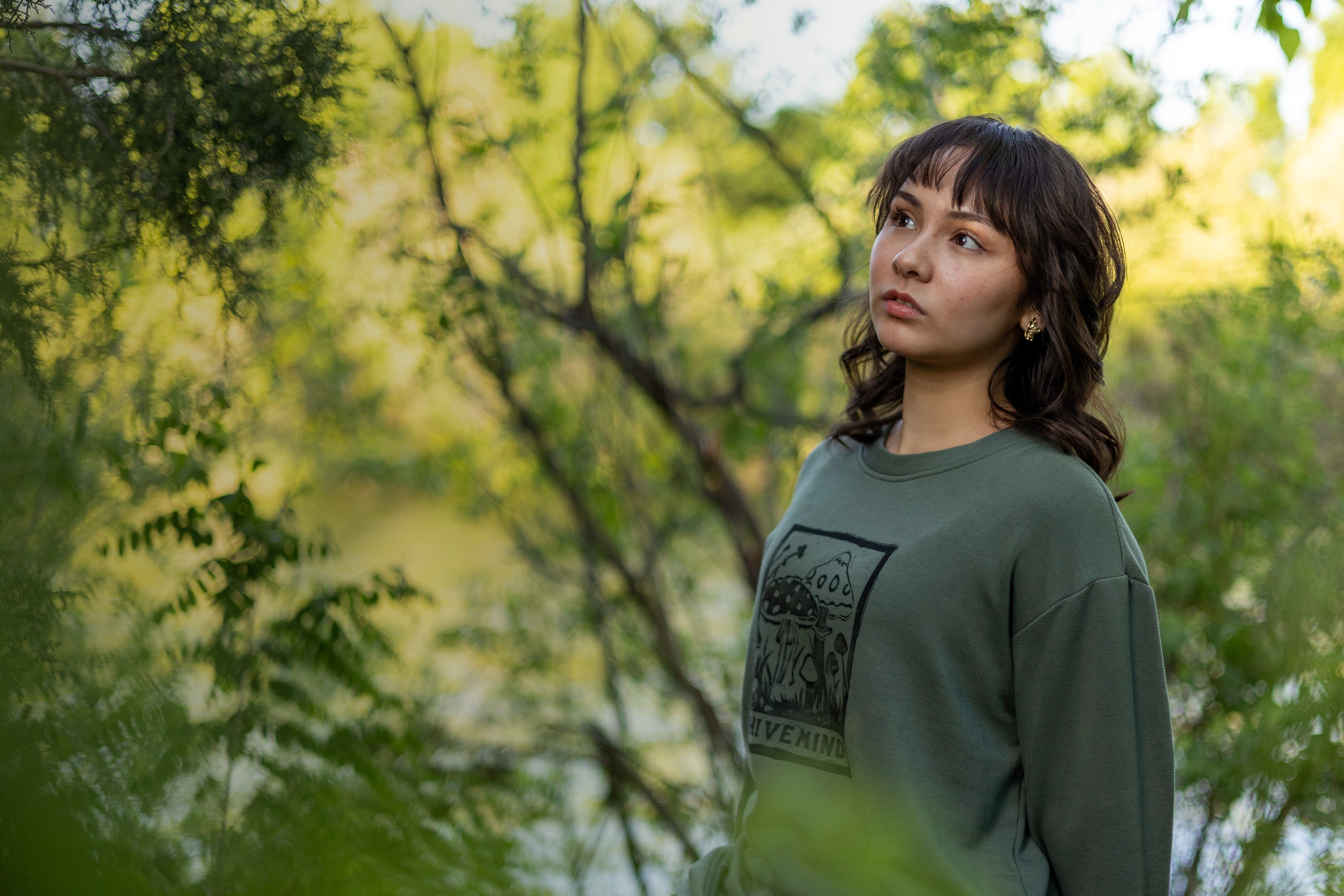 Woman in a green sweatshirt sitting among trees with a blurred background