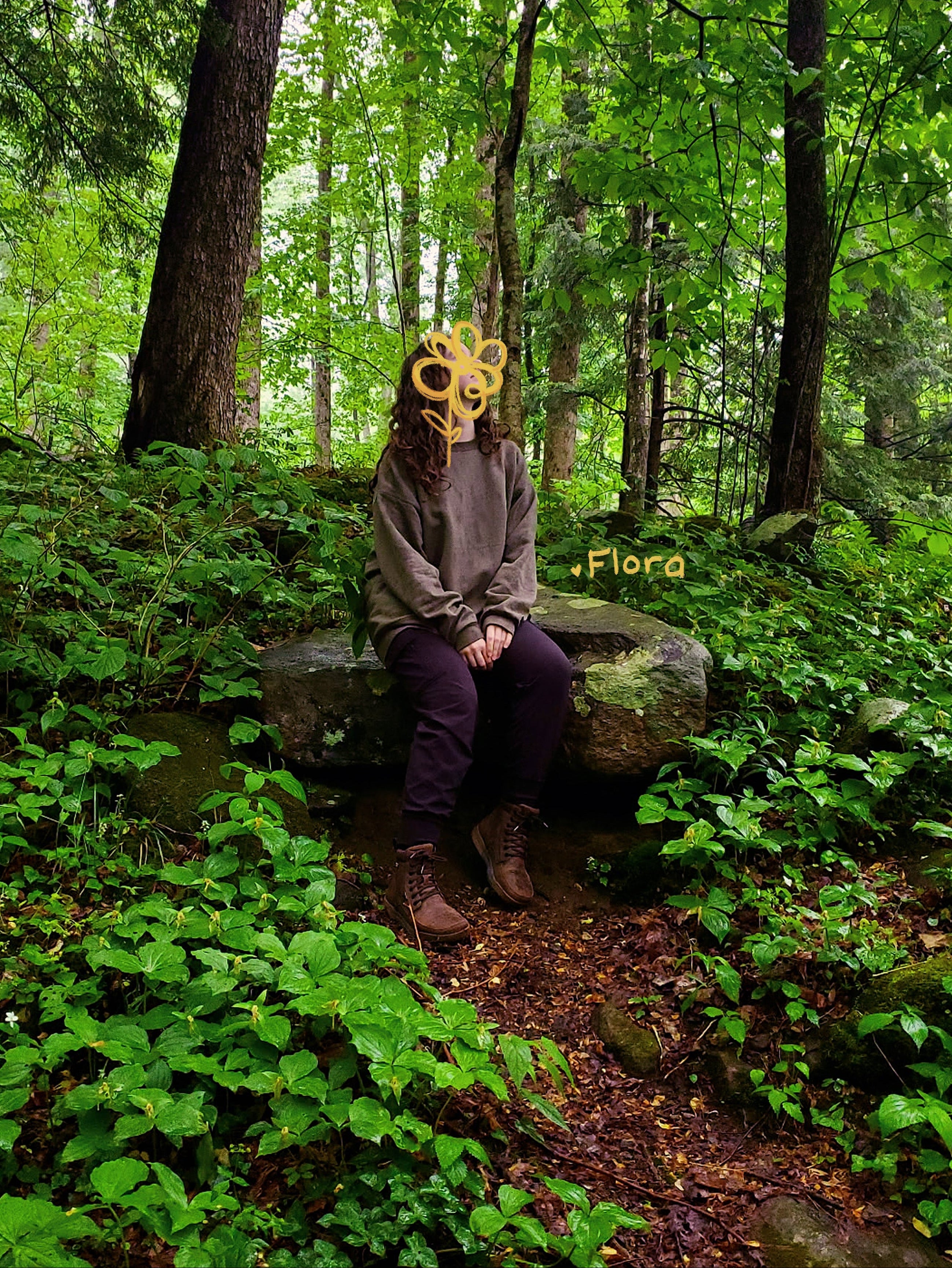 Person wearing a yellow flower mask sitting on a rock in a forest